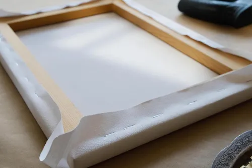 Canvas being stretched and stapled onto a wooden stretcher frame