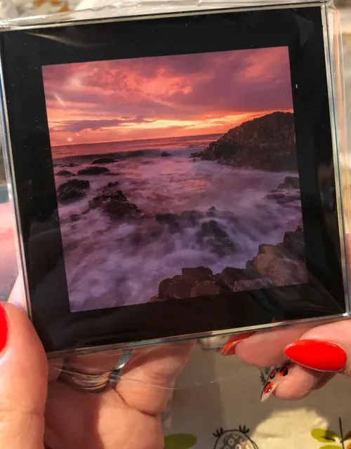 Glass photo coaster with a sunset seascape print held in a hand